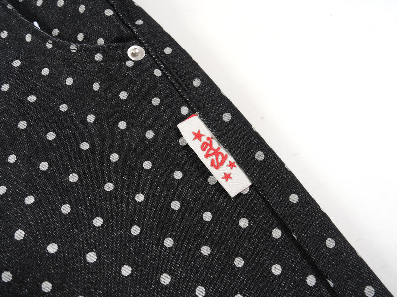 Side seam detail with small white fabric label on black polka-dot denim pants