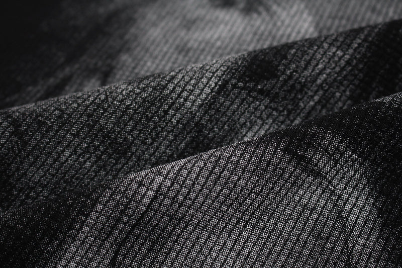 Close-up of black textured fabric with a subtle shadow portrait graphic on a studded mock-neck tee