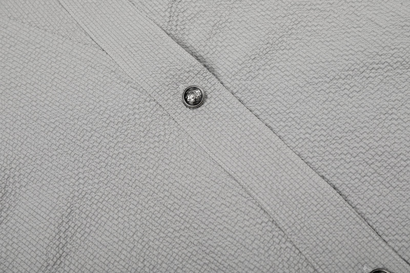 Close-up of a light gray textured asymmetrical cotton shirt with diagonal seam and decorative metal button