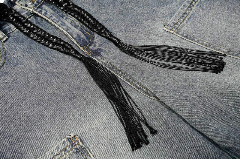 Close-up of black braided waist ties on blue jeans with frayed tassel ends