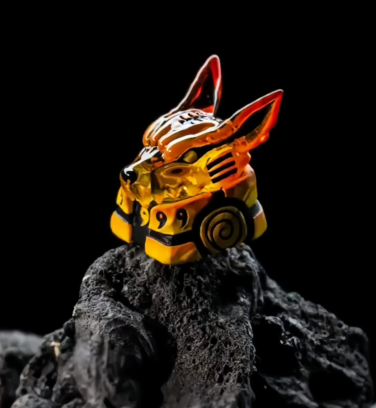 A fox-themed figurine, resembling a piece from the Naruto Ninja Keycaps Set with scrolls, tailed beasts, and Kurama designs, is intricately designed in orange and yellow colors with sharp ears and a spiral symbol while sitting on a textured black rock.