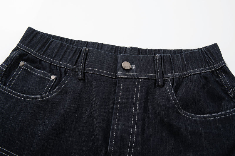 Close-up of the waistband and front pockets on dark denim jeans with contrast stitching