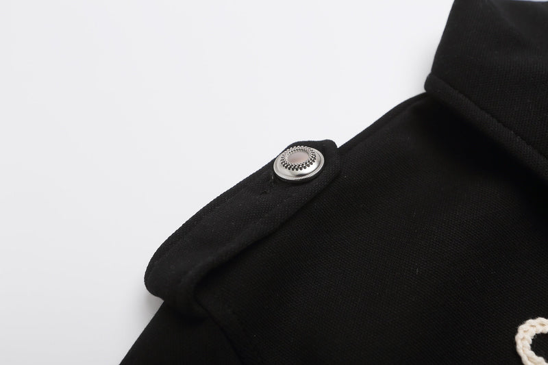 Black polo shirt close-up with silver military-style shoulder button and braided rope embroidery detail