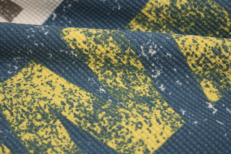 Close-up of blue waffle knit fabric with yellow and green abstract graphic pattern and textured streetwear detail