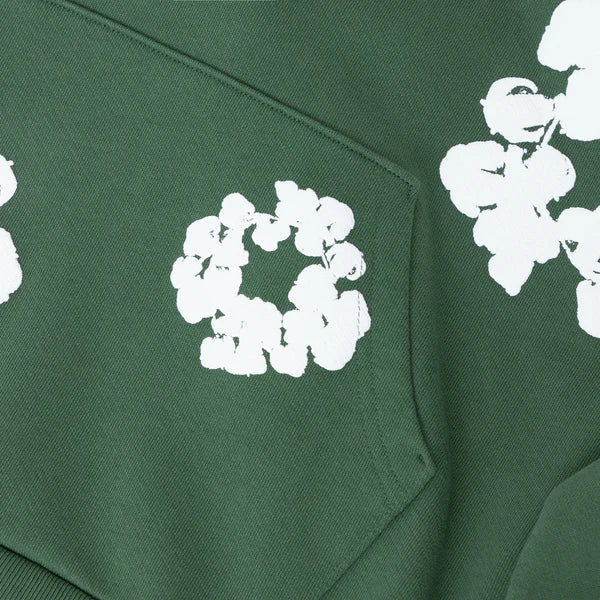 A close-up of the Forest Green “Cotton Wreath” Denim Tears Hoodie, a cotton fleece pullover featuring a front pocket and scattered white floral prints for streetwear style.