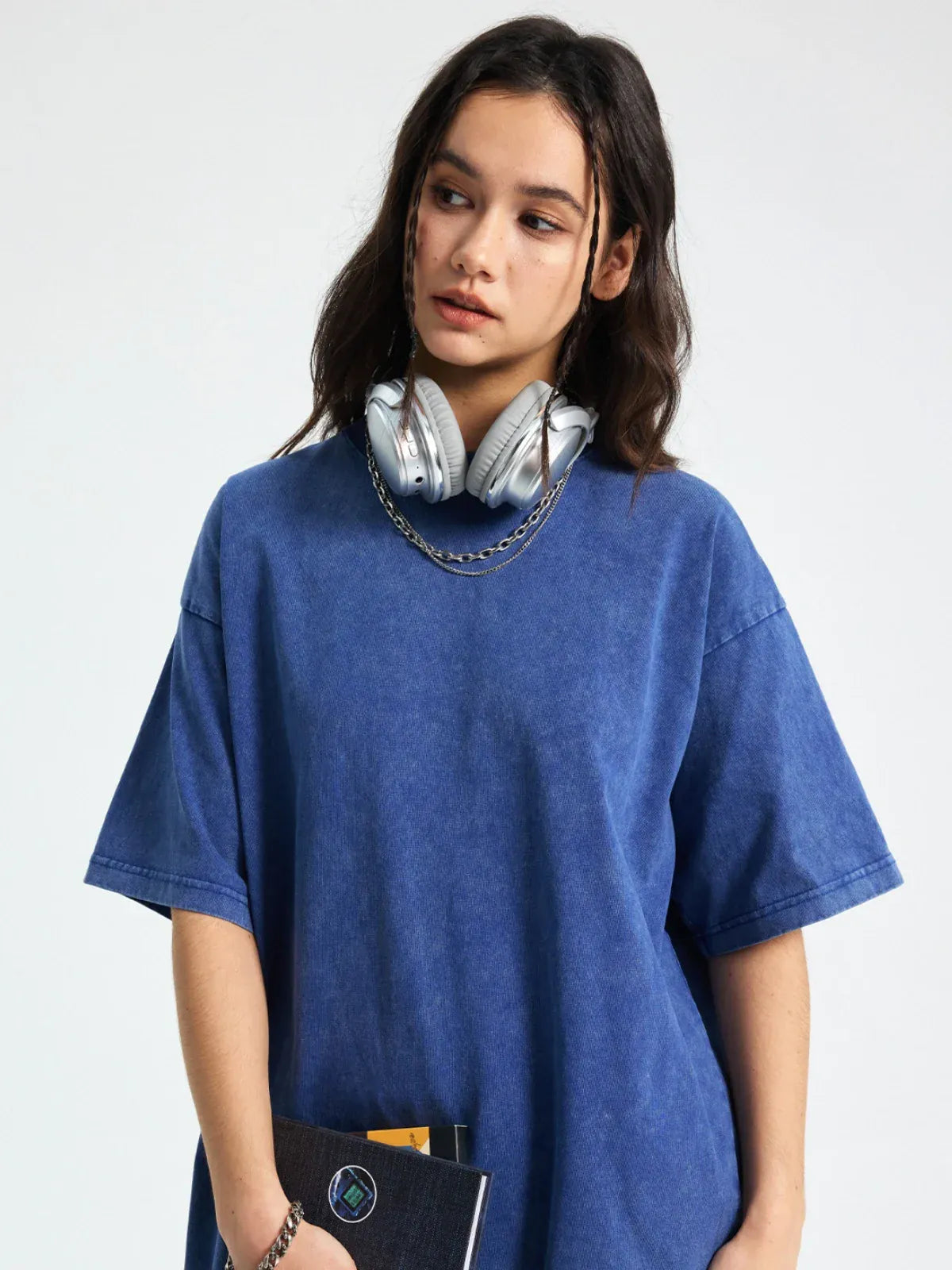 A young woman in a Custom Anime Character Periwinkle Blue Washed T-Shirt with headphones around her neck holds a notebook while looking to the side.