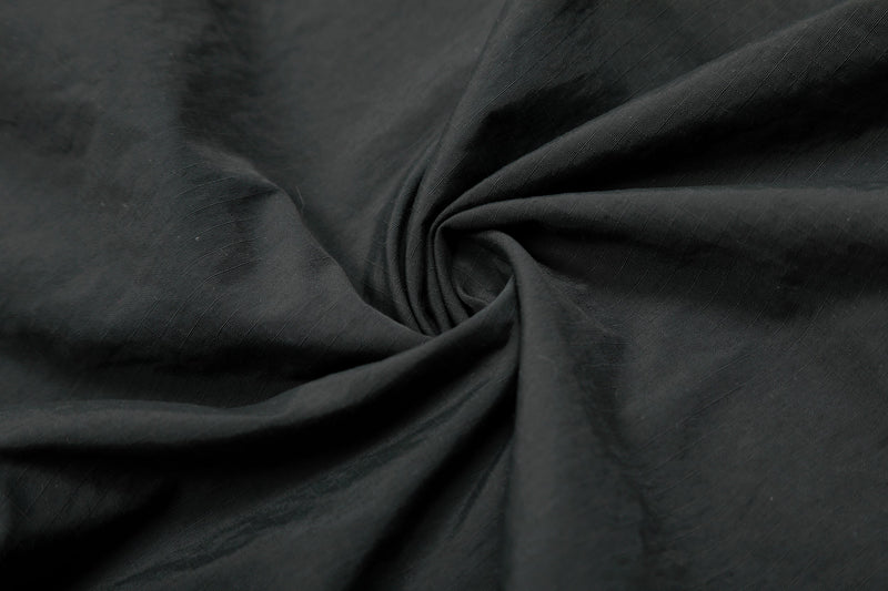 Close-up of black nylon fabric with a smooth, matte finish and subtle ripples for a varsity streetwear jersey
