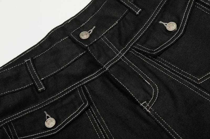 Close-up of front waist details on black denim pants with contrast stitching and metal buttons