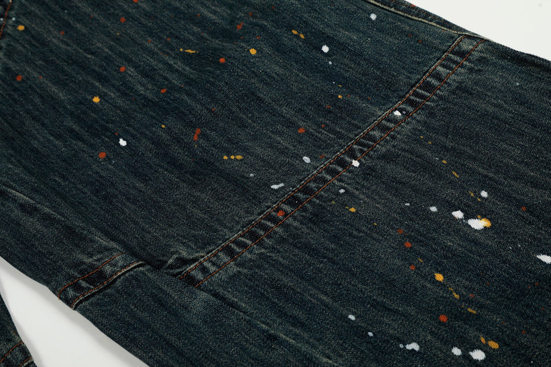 Close-up of denim leg with diagonal seam and scattered paint splatter