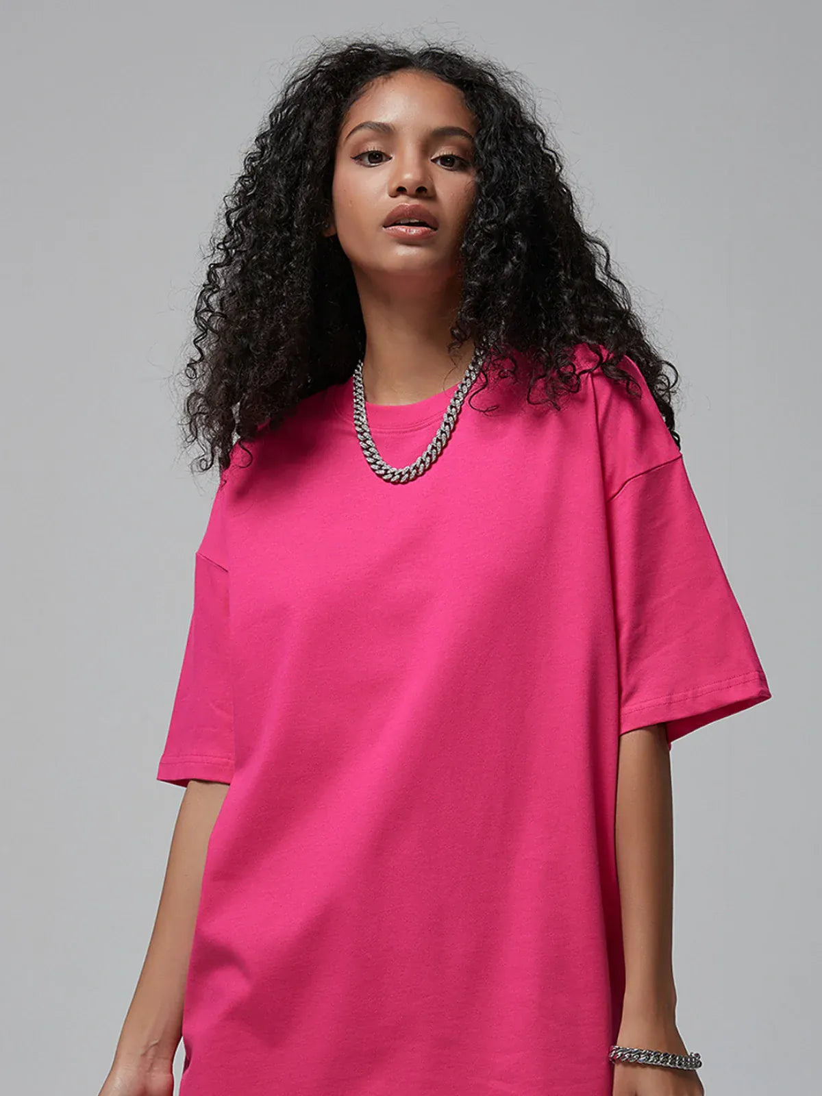 A woman with curly hair wears the Custom Anime Character Hot Pink T-Shirt—Personalized 230GSM 100% Cotton Tee—and a silver chain necklace, standing against a plain gray background.