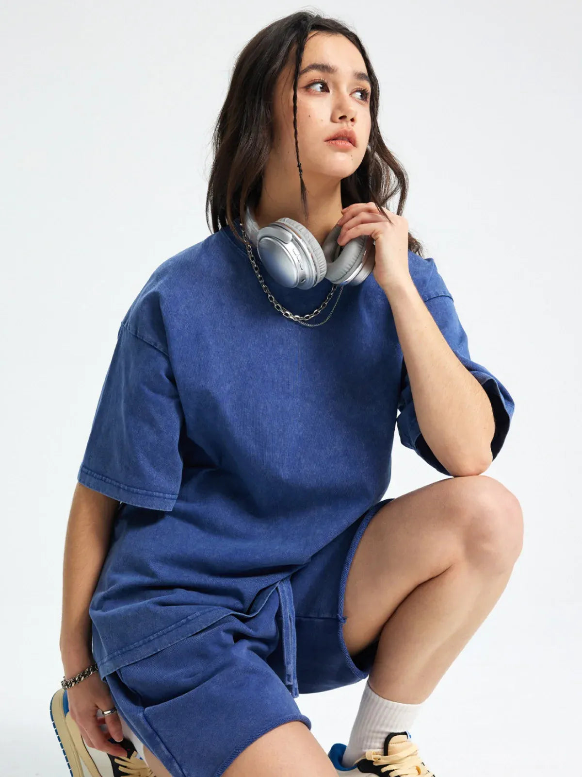 A woman kneels on one knee, looking to the side with headphones around her neck, wearing the Custom Anime Character Periwinkle Blue Washed T-Shirt – a personalized anime style tee.