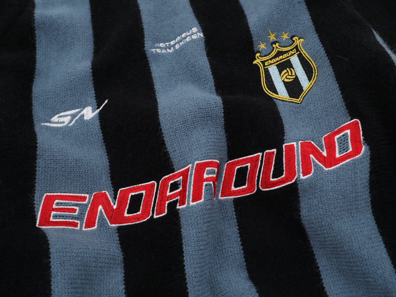 Close-up of front stripes, ENDAROUND logo, and embroidered crest on black knit sweater