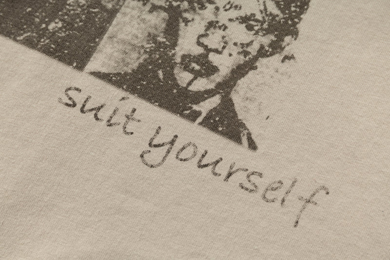 Close-up of a beige streetwear tee with a distressed black portrait graphic and handwritten No Comment text