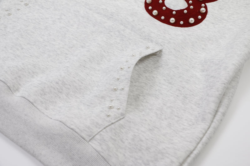 Close-up of light gray hoodie pocket and hem with pearl stud trim