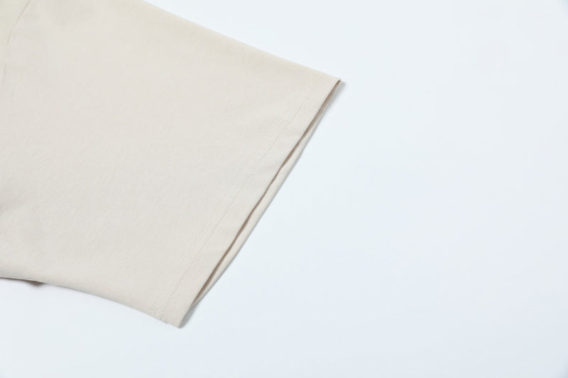 Close-up of a cream minimalist tee sleeve with clean seam detailing on a white background