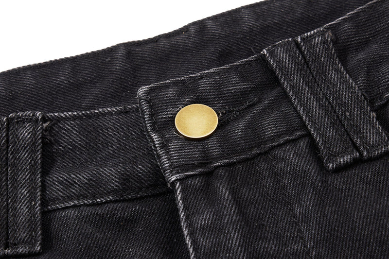 Close-up of black denim waistband with a gold button and belt loop details