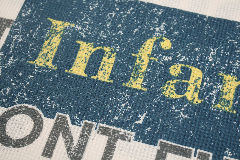 Close-up of blue and yellow distressed 'Infant' print on waffle-knit shirt