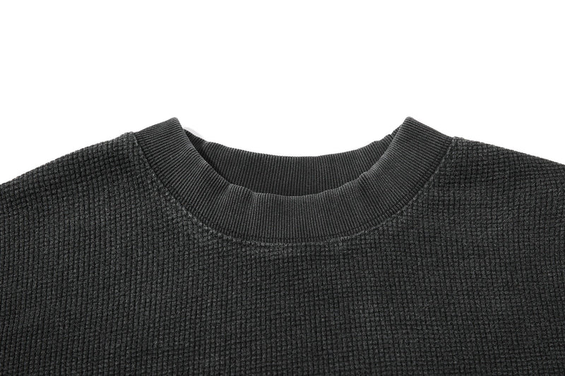 Close-up of a dark waffle knit graphic T-shirt with a ribbed crew neckline and vintage washed texture