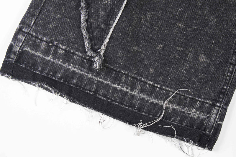 Close-up of frayed hem on black wide-leg jeans with faded wash and raw edge stitching