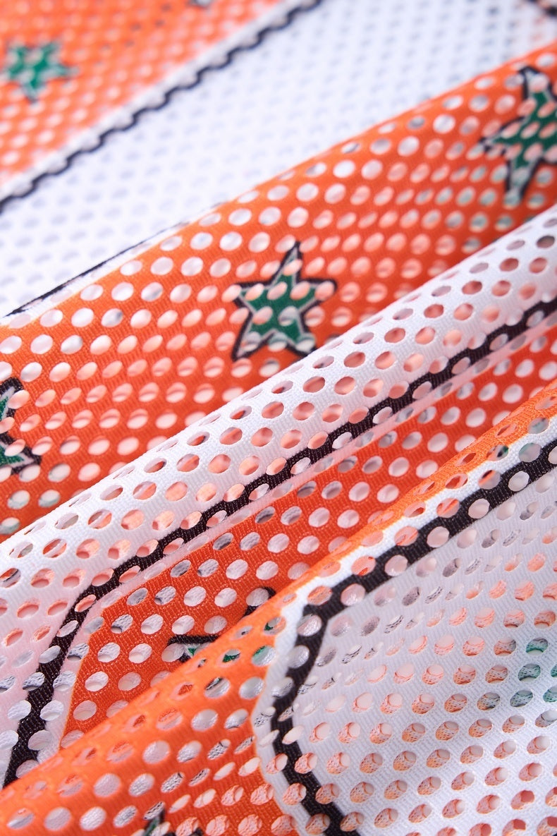 Close-up of orange and white mesh jersey fabric with star detail and perforated retro streetwear texture