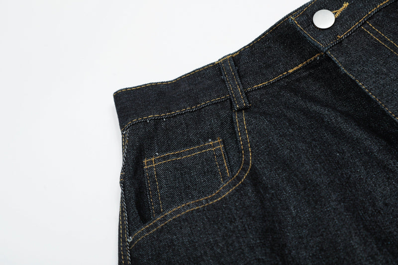 Close-up of black denim front waistband with snap button and stitched coin pocket