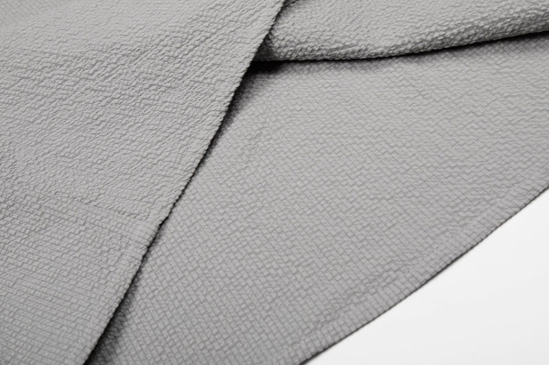 Close-up of textured gray cotton shirt fabric with layered asymmetrical seams and a minimalist streetwear look