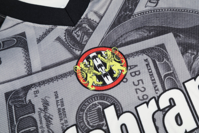 Close-up of a mesh football jersey with dollar bill print and a bold red and yellow crest on gray fabric