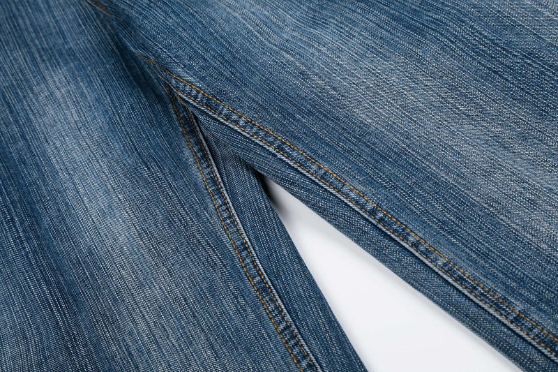 Close-up of the denim leg fabric and seam stitching on faded blue jeans