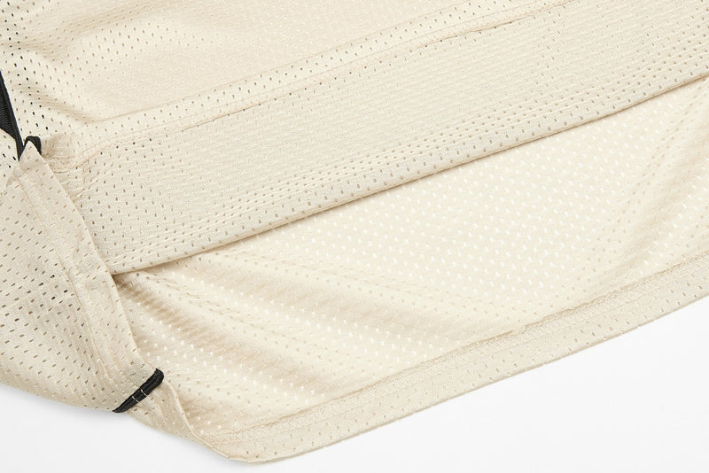 Close-up of a beige mesh jersey hem with perforated fabric, black trim, and stitched detailing
