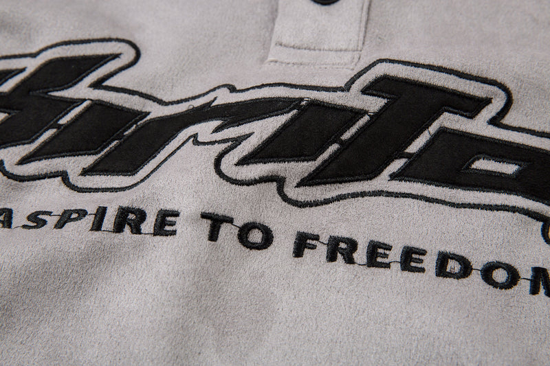 Close-up of embroidered front graphic and slogan on the light gray polo shirt
