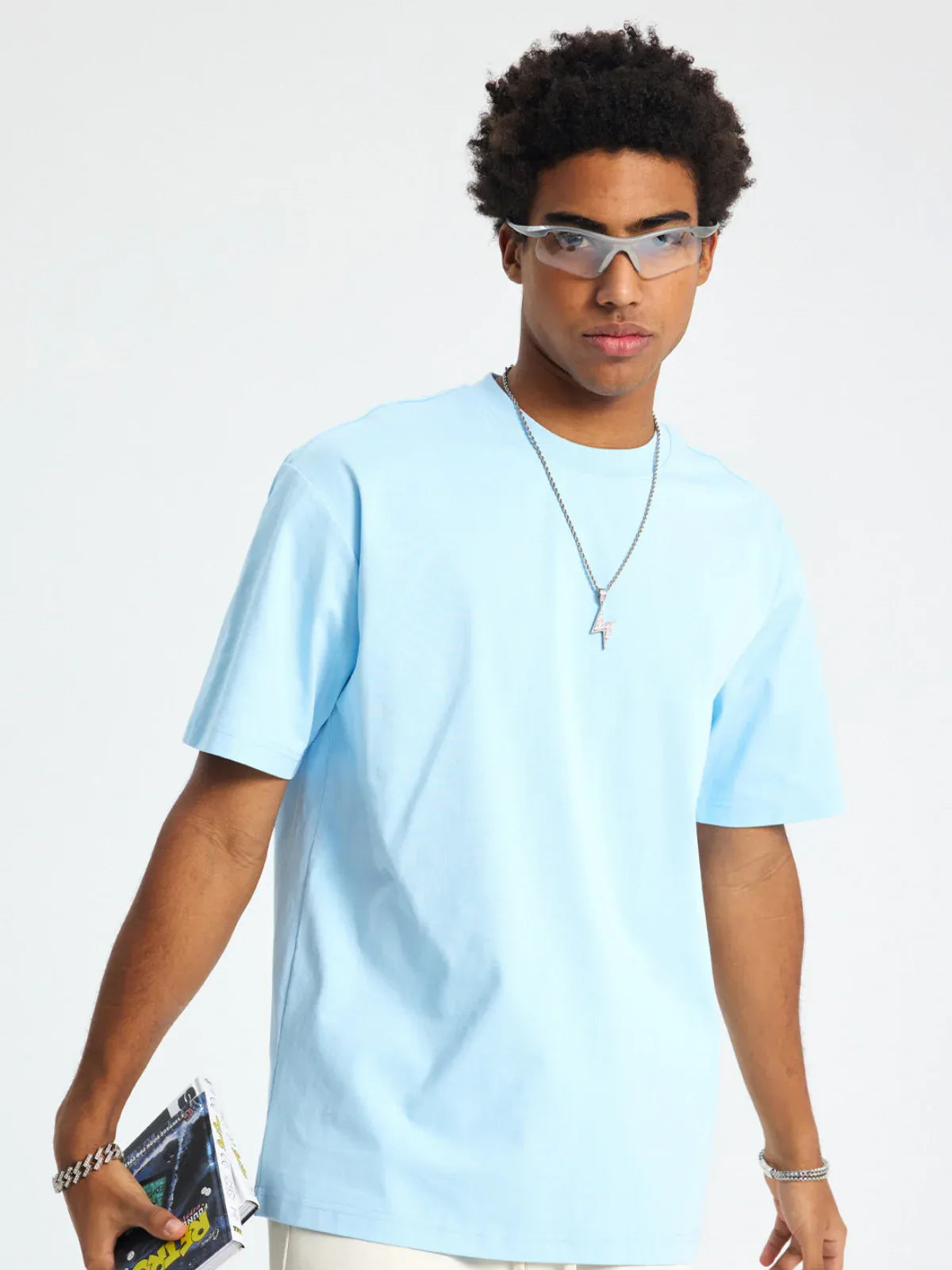 A person wearing the Custom Anime Character Sky Blue T-Shirt (230GSM 100% cotton), along with glasses and a necklace, stands against a plain background holding a small item in their right hand.