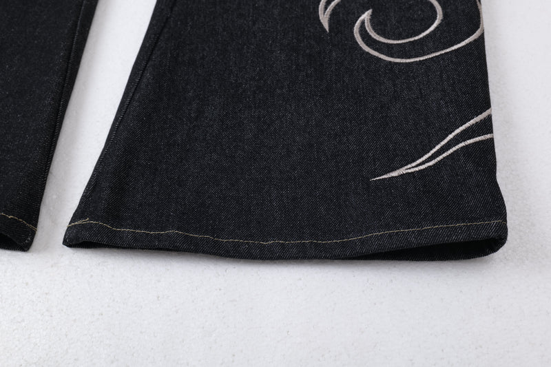 Close-up of the bottom hem on dark denim jeans with embroidered swirl detail
