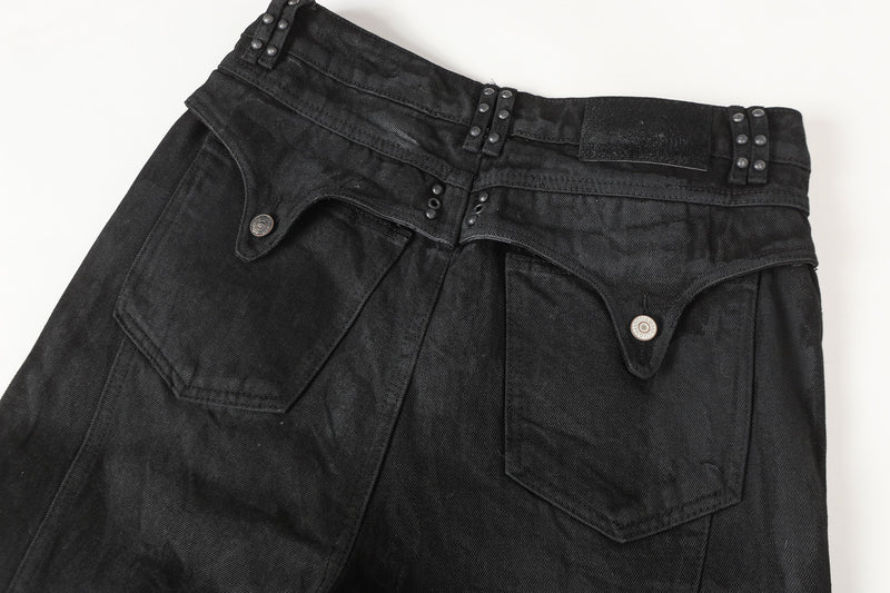 Close-up of black denim waistband with metal studs, belt loops, and front pocket flap