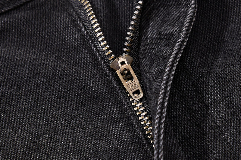 Close-up of metal zipper pull on black denim with visible stitching