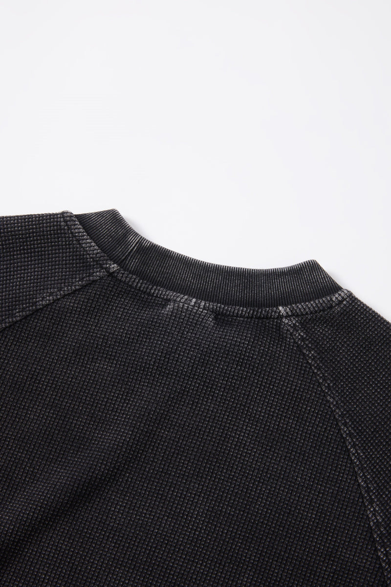Close-up of a black textured crewneck T-shirt with ribbed collar against a clean white background