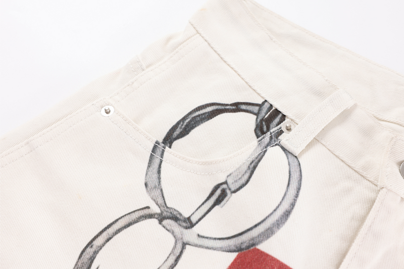 Close-up of chain graphic on cream jeans near the back pocket