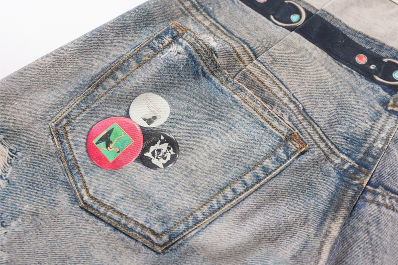 Back pocket close-up with three graphic patches on faded blue denim