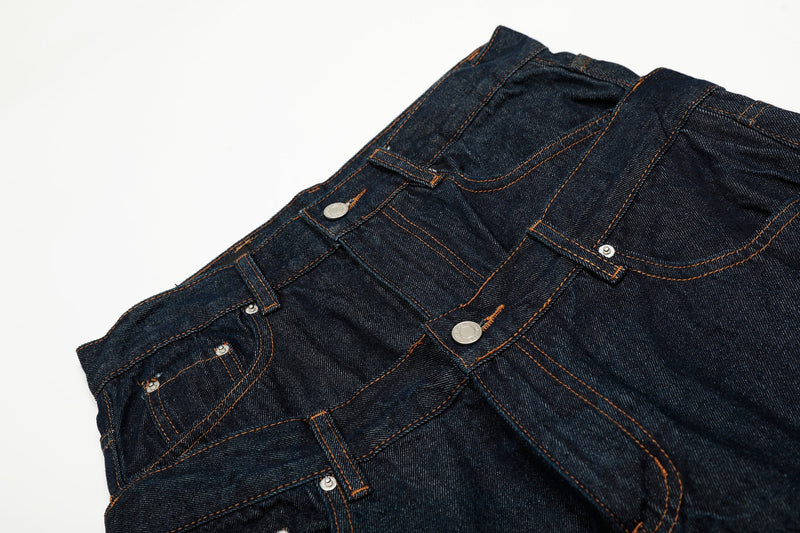 Close-up of the front waist on deep indigo jeans showing layered bands, snaps, and stitching