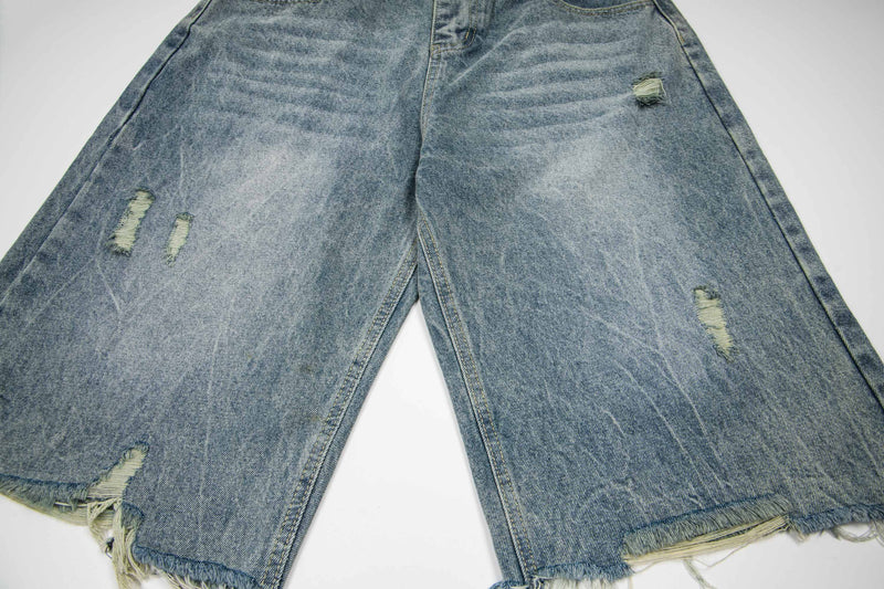 Front view of distressed light wash denim shorts with frayed hems and ripped patches
