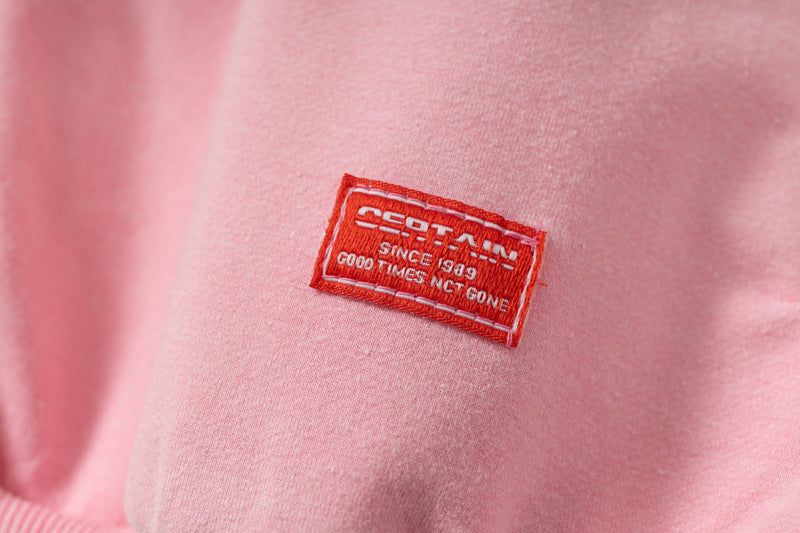 Close-up of red woven logo patch on pink hoodie chest