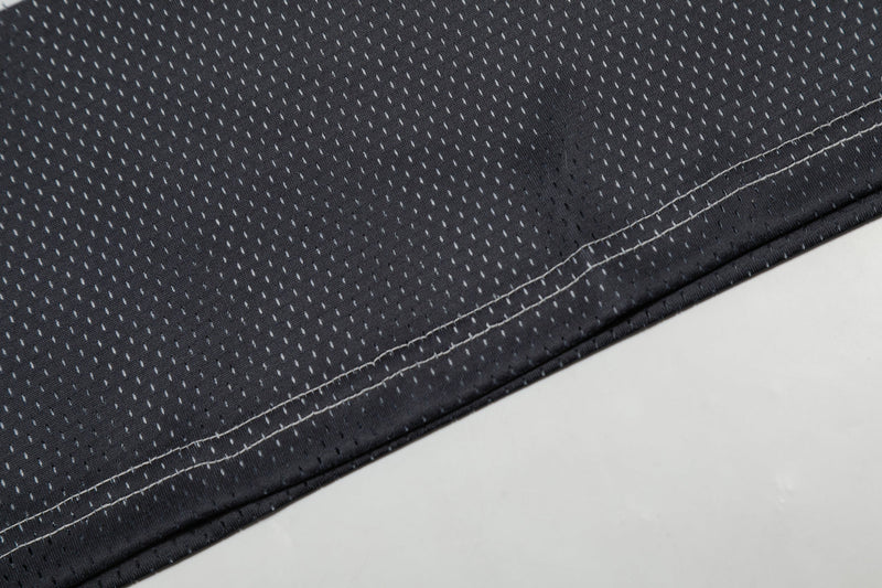 Close-up of black mesh football jersey fabric with white stitched hem and perforated texture
