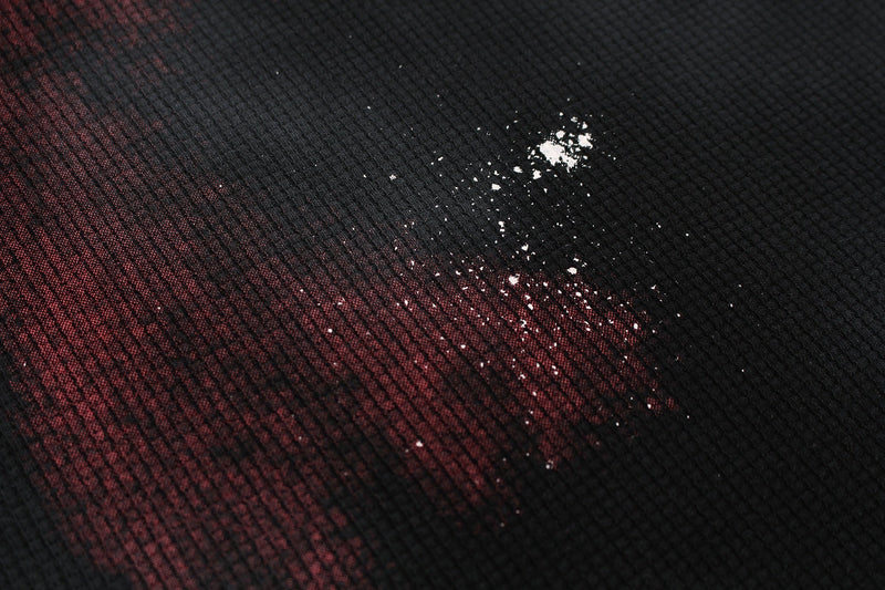 Close-up of black and burgundy washed tee fabric with distressed white speckle print and textured oversized streetwear style