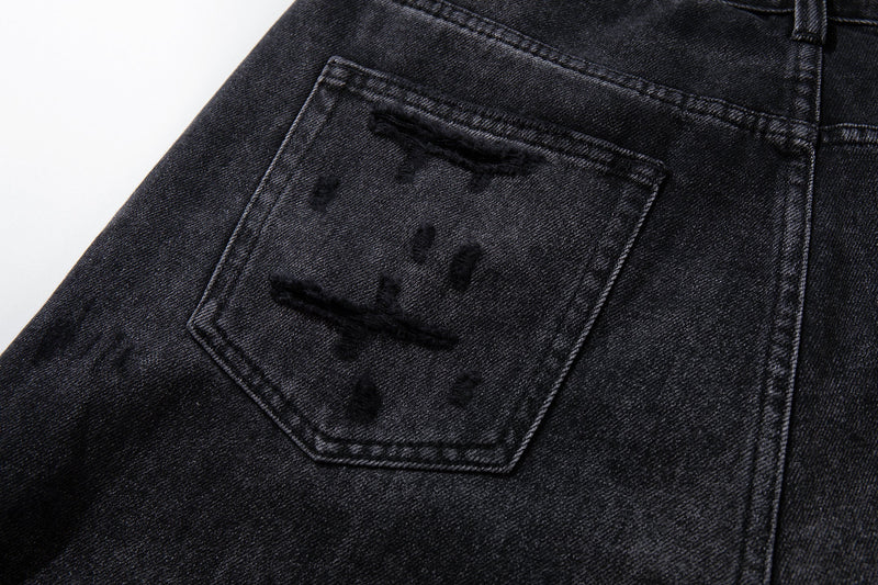 Close-up of back pocket on deep charcoal jeans with distressed tear details
