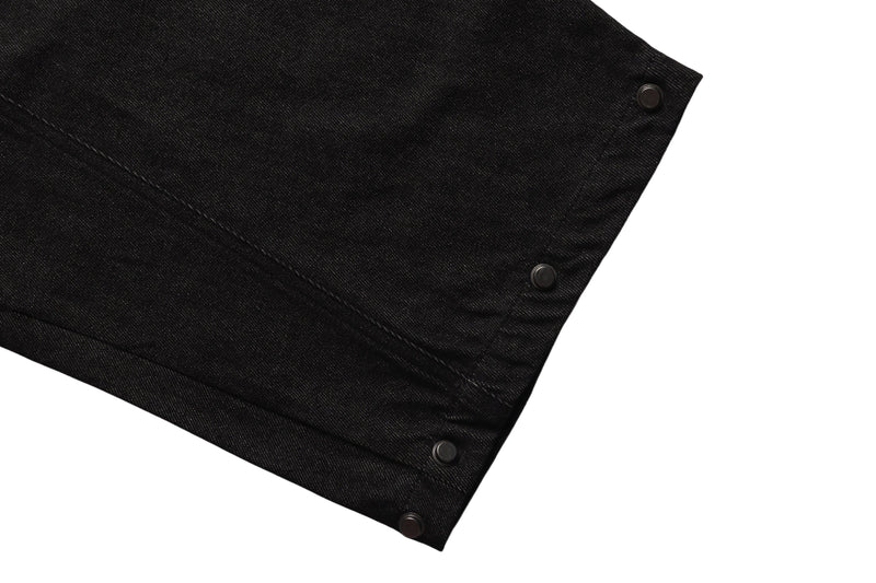 Close-up of black denim pant leg side seam with snap buttons
