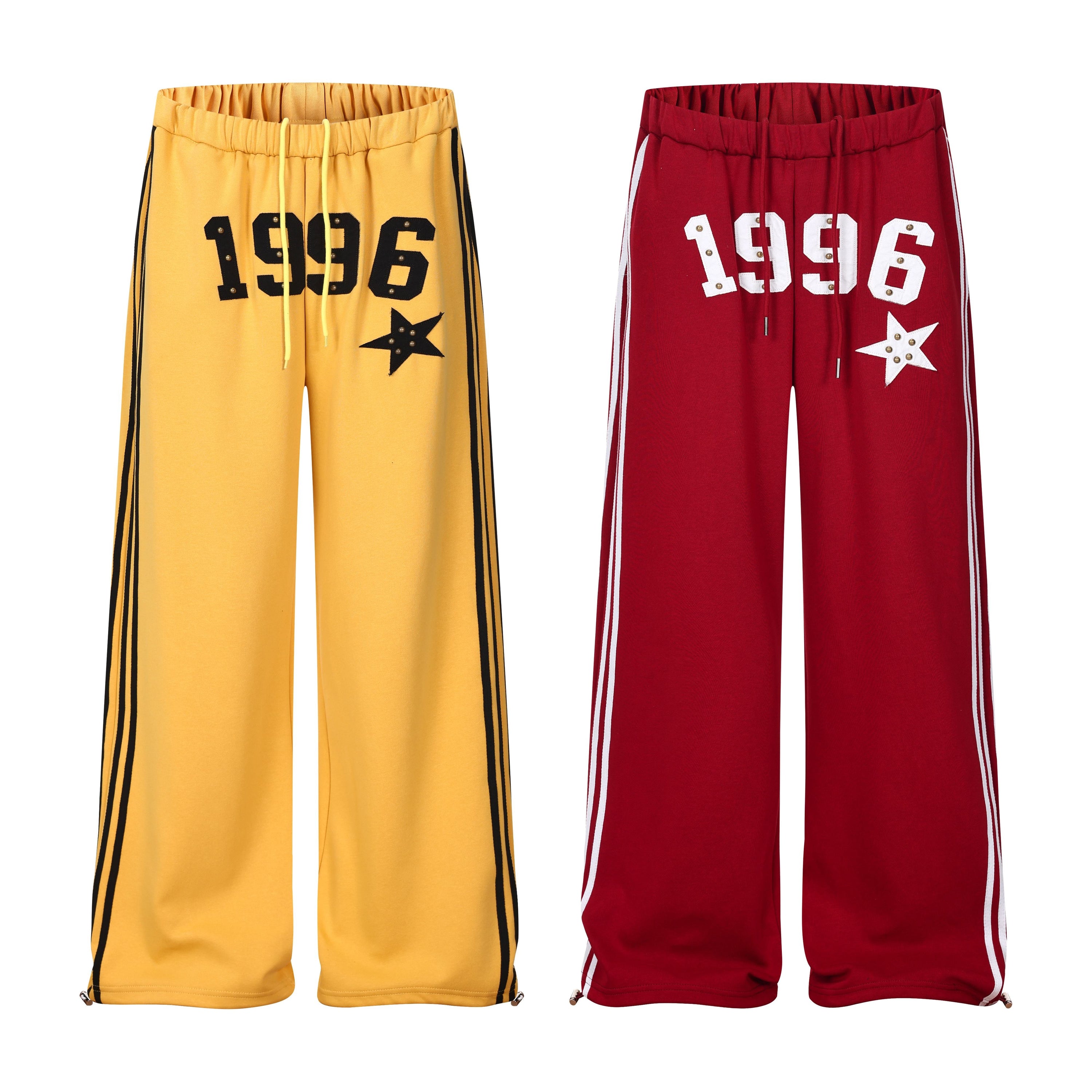 Yellow wide-leg varsity track pants with black 1996 lettering, star appliqué, and contrast side stripes on white background