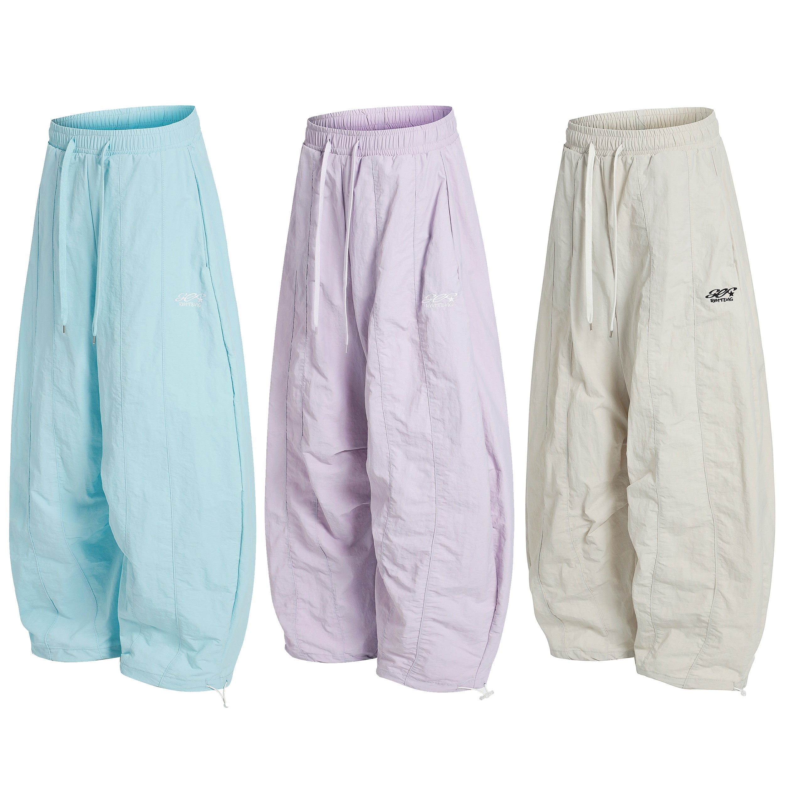 Three pairs of oversized pastel nylon stacked pants in sky blue, lilac, and cream with elastic waistband and adjustable hems