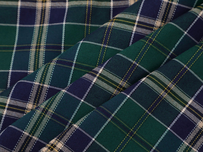 Close-up of green and navy plaid shirt fabric with white and yellow lines, featuring a rugged streetwear pattern
