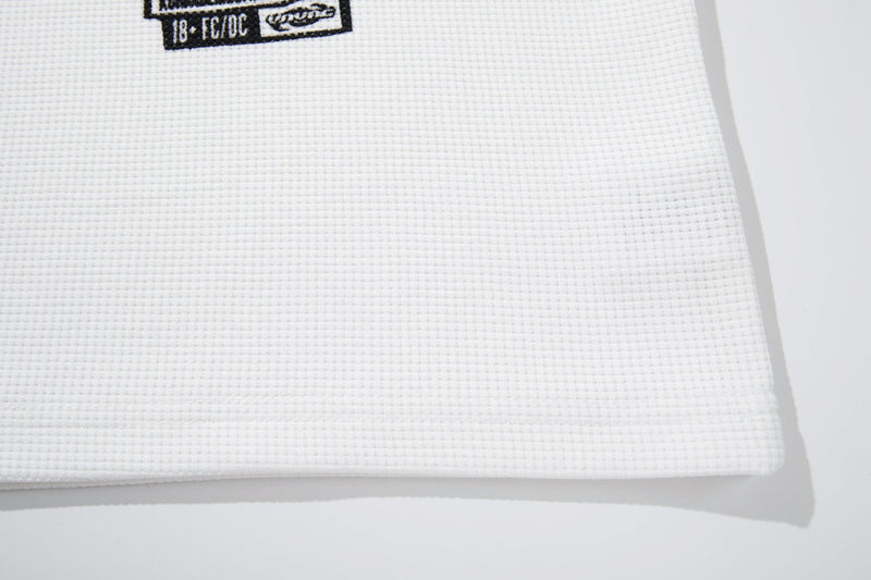 White waffle-knit graphic tee with a cropped hem and subtle black street-style print detail near the neckline
