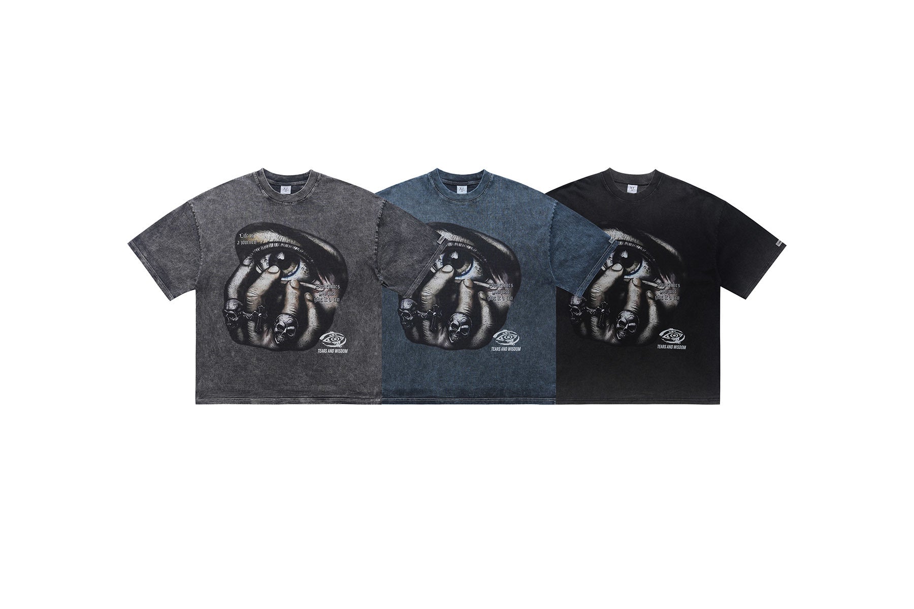 Three vintage-washed graphic tees in grey, blue, and black featuring a surreal eye and skull hand print with Tears and Wisdom