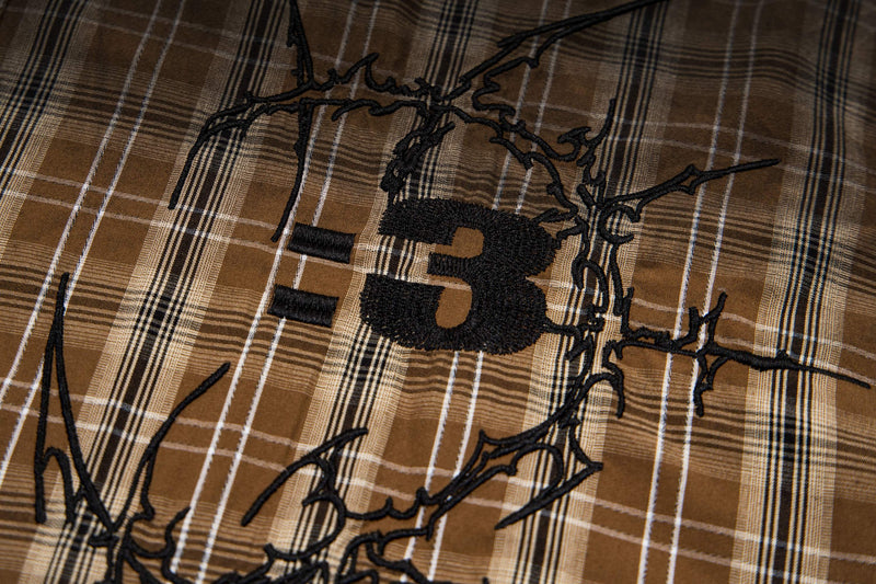 Close-up of a brown plaid vintage shirt with black embroidered graphic lettering and distressed streetwear detailing